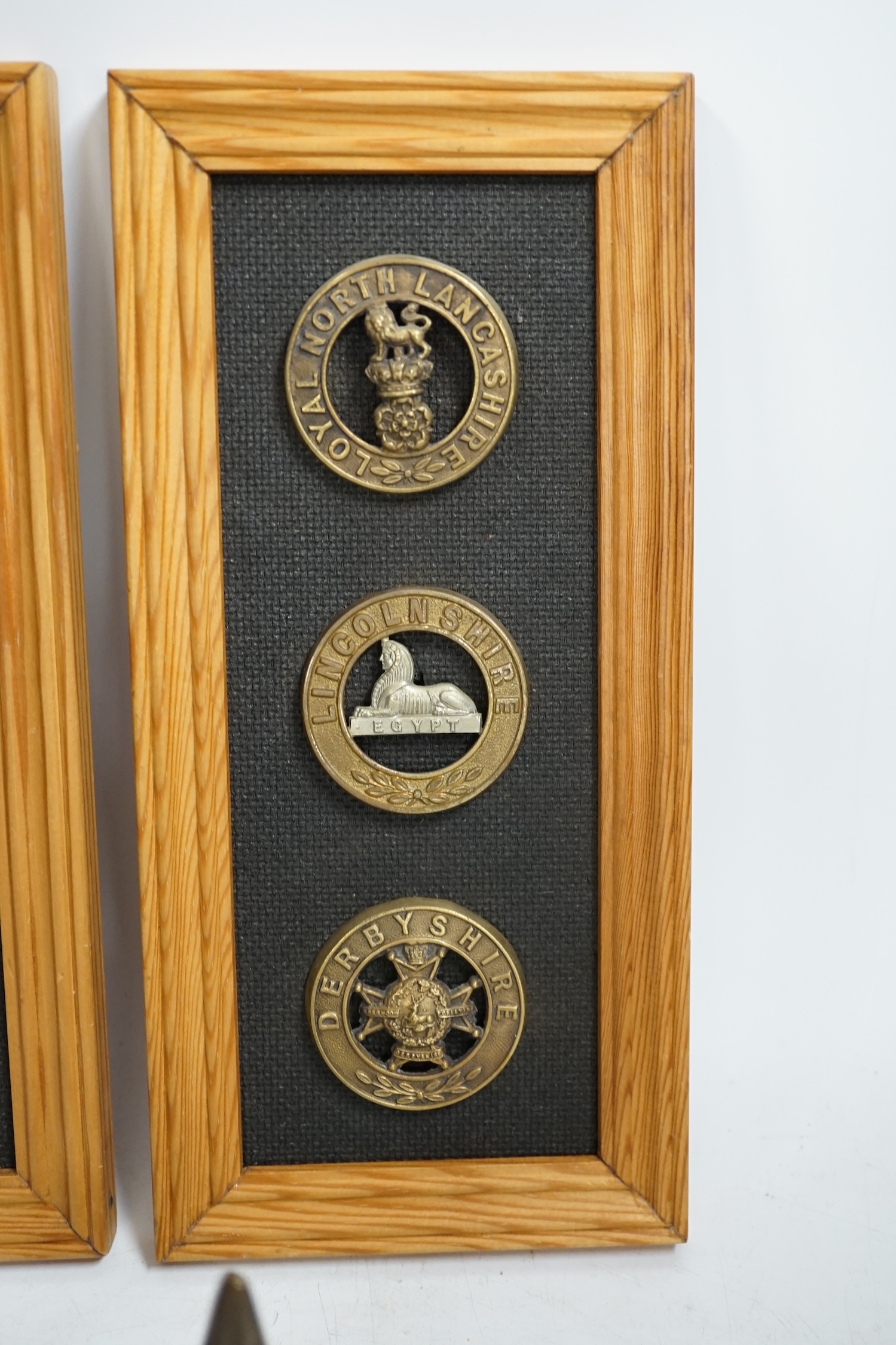 Six military helmet plates mounted on two boards, together with two helmet spikes and a cap badge, including; the Yorkshire Regiment, the Royal Guernsey Light Infantry, the Loyal North Lancashire, the Lincolnshire Regime